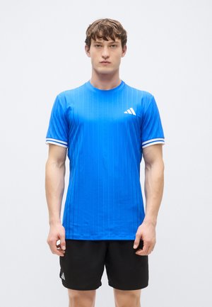 Blauw sportshirt met verticale strepen, ronde halslijn en mouwen met witte accenten. Draagt daarbij zwarte shorts met logodetails.