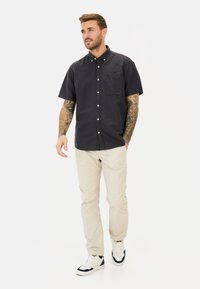 Korte mouwen marineblauw shirt met een borstzak, beige broek en witte sneakers met zwarte accenten. Model staat en loopt.