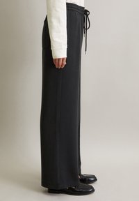 Schwarze, hochtaillierte Hose mit elastischem Bund, Kordelzug und Seitentaschen. Glatte Textur, gerade Beinform und Volllänge.