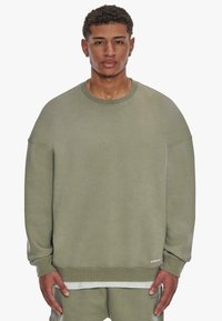 Olivenfarbener, übergroßer Pullover mit Rundhalsausschnitt und Fallerschultern. Weiches Baumwollmaterial, gerippte Bündchen und Saum.