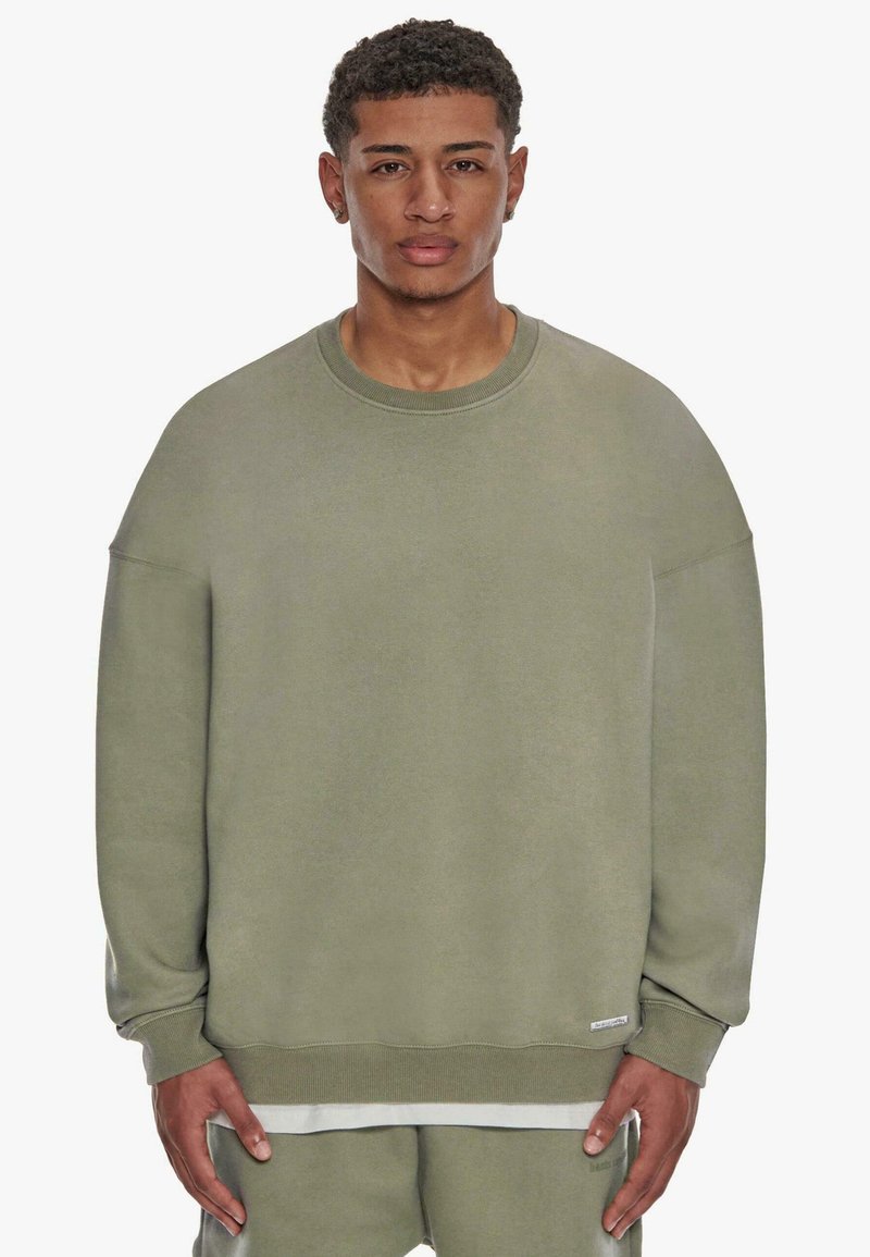 Olivenfarbener, übergroßer Pullover mit Rundhalsausschnitt und Fallerschultern. Weiches Baumwollmaterial, gerippte Bündchen und Saum.