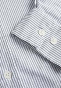 Weiß- und grau gestreifter Hemdblusenkragen mit zwei weißen Knöpfen. Baumwollstoff, glatte Textur, schmale Streifen, saubere Nähte und Detail mit geknöpftem Manschettendesign.