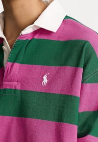 Gestreiftes Rugby-Shirt mit abwechselnd grünen und rosa horizontalen Streifen, einem weißen Kragen und einem kleinen gestickten Logo auf der Brust.
