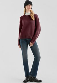 Bordeaux gebreide trui met een hoge hals, gecombineerd met slim-fit blauwe jeans en zwarte enkellaarsjes, met zilveren hardware accenten.