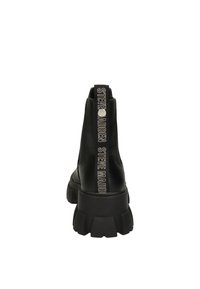 Bottines noires avec une semelle épaisse, finition en cuir lisse et une boucle distinctive à l'arrière portant "STEVE MADDEN" en lettres bold.