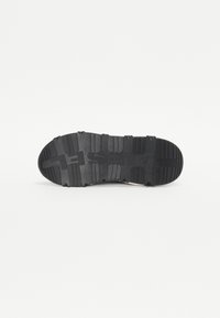 Black rubber shoe sole with textured pattern, featuring prominent ridges and a logo. Flat with slight curve towards the toe.