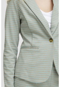 Svetle modrý kostkovaný blazer s hnědými akcenty, jednořadým zapínáním na knoflík, klopami a slim fit střihem. Obsahuje náprsní kapsu a strukturovanou tkaninu.