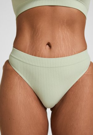 Gros plan sur le torse et le haut des cuisses d’une personne portant des sous-vêtements côtelés vert clair et un crop top, montrant des vergetures visibles sur la peau.