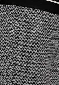 Black and white houndstooth patterned pants with a black waistband featuring two thin white stripes.