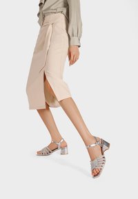 Gonna midi beige con spacco laterale e vita legata, abbinata a sandali con tacco a strappo argentati con dettagli in strass e tacchi a blocco.