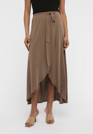 Jupe longue à enrouler en tissu brun clair avec une texture lisse. Présente une taille à nouer et un ourlet asymétrique. Associée à des chaussures à talons carrés nude.