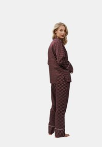 Completo pigiama borgogna con pois bianchi, composto da una camicia a maniche lunghe con bottoni e pantaloni coordinati, rifiniti con dettagli bianchi.