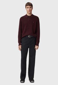 Burgundy long-sleeve polo with a collar and three buttons, paired with black trousers; the belt is black with a silver buckle.