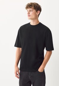 Fekete pamut rövid ujjú póló, kerek nyakkivágással, laza szabással és sima tapintású anyaggal, sötétszürke farmerrel viselve.