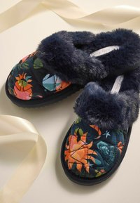 Sininen patchwork-kangastossu, jossa on värikkäitä kukkakuoseja ja pehmeä tekoturkisreunus. Rakeinen pohja lisää pitoa.