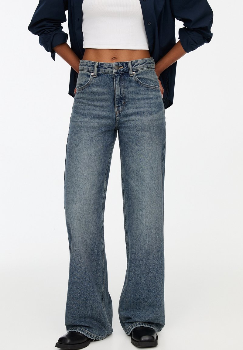 Lahjakkaat siniset farkut, joissa on korkea vyötärö, klassinen viisi-taskuinen muotoilu ja hienovarainen kuluminen tekstuurin luomiseksi.