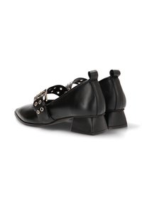 Zapatos de cuero negro con punta cuadrada, tacón bloque y una correa decorativa con tachuelas metálicas. El diseño incluye dos lengüetas traseras para tirar.