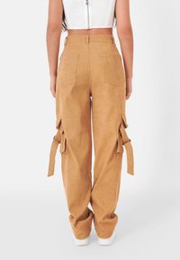 Lichtbruine corduroy cargobroek met grote zijzakken, verstelbare banden en een relaxte pasvorm. Witte sneakers maken de look compleet.