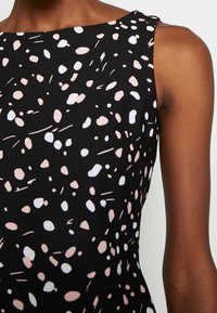 Svart ärmlös klänning med färgglad prickig mönster i rosa och vitt, med ett slätt tyg och en något åtsittande design.