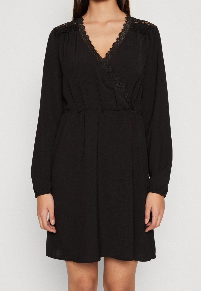 Robe noire en tissu léger avec des manches longues, un bord en dentelle au niveau du décolleté et une taille cintrée pour un ajustement décontracté.