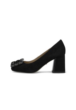 Zapato de salón negro de ante con tacón grueso y una gran hebilla decorativa negra en la puntera.