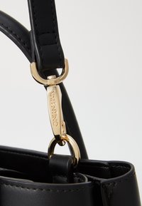 Correa de bolso de cuero negro con herrajes dorados y un gancho de botón. Presenta una etiqueta con la marca "Valentino" grabada en ella. Textura suave.