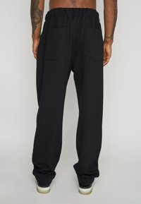 Sorte sweatpants med en samlet talje, to store påsyede lommer på bagsiden og en afslappet pasform. Stoffet ser blødt og glat ud.