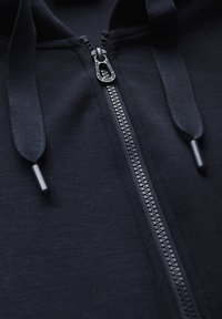 Black zip-up hoodie featuring a smooth fabric texture, contrasting zipper, and drawstrings. Detailing includes a molded zipper pull.