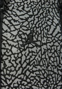 Saco de tecido texturado a preto e branco com um logo Jumpman preto proeminente e padrão abstrato, com alças pretas elegantes.