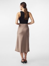 Zwarte mouwloze top gecombineerd met een midi-lange, beige satijnen rok, met een gladde textuur en een vloeiend ontwerp. Draagt zwarte hakken.