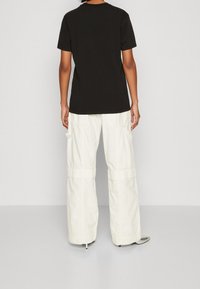 Svart bomull t-shirt med korta ärmar, kombinerad med vida vita cargobyxor som har sidofickor och en avslappnad passform. Platta skor synliga.