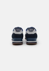 Para granatowo-szarych sneakersów z nadrukiem "1973" na piętach, wyeksponowanych od tyłu na białym tle.