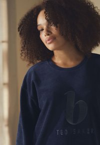 Felpa blu navy con texture a coste, con logo nero in rilievo "b" e scritta "TED BAKER" in basso. Design con collo rotondo.