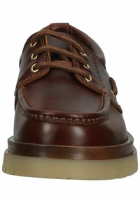 Braune Lederschuhe mit abgerundeter Spitze, zwei Paar Metallösen, braunen Schnürsenkeln und einer sandfarbenen Gummisohle. Die Nähte betonen die Designdetails.