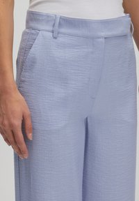Lichtblauwe, gestructureerde broek met een vlakke voorkant, zijzakken en een rechte pijpdesign. Ontworpen met een subtiele glans en details aan de tailleband.