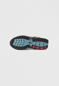 Sola da sapatilha Nike com um fundo de borracha preta, almofada turquesa e botões de destaque vermelhos. O padrão de piso inclui designs circulares e retangulares.