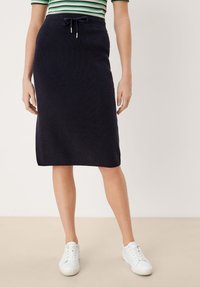 Marineblauwe geribbelde gebreide rok met een trekkoord in de taille, tot op de knieën, gecombineerd met witte sneakers. Glad oppervlak, minimalistisch ontwerp, zonder patronen.