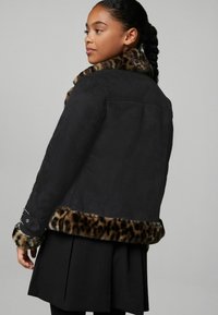 Sort jakke med leopardprint faux fur krave og manchetter, der har en glat tekstur og struktureret design. Indeholder dekorativ hardware på ærmerne.