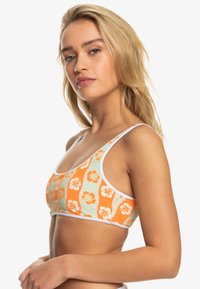 Oranje en groene sportbeha met bloemmotief en witte accenten. Gemaakt van textuurstof, met dunne schouderbanden en een naadloos ontwerp.