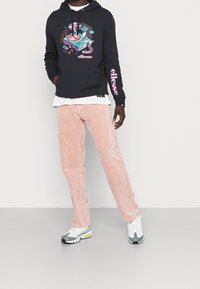 Sudadera negra con un diseño gráfico colorido, acentos rosas en las mangas; pantalones de pana color rosa claro; zapatillas grises y blancas.
