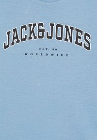 Šviesiai mėlynas medvilninis marškinėlis su ryškiu juodu "JACK & JONES" logotipu viršuje ir smulkesniu tekstu "EST. 90 WORLDWIDE". Minkšta tekstūra, kasdieniškas stilius.