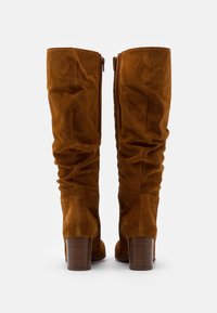Brązowe zamszowe kozaki do kolan na płaskim obcasie, z bocznym zamkiem błyskawicznym i marszczonym wykończeniem wzdłuż cholewy.