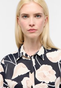 Chemise à boutons avec un fond sombre et de grands motifs floraux en beige doux et rose. Fabriquée en tissu léger avec un col classique.