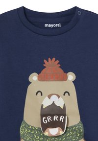T-shirt in cotone blu navy con un'illustrazione di un orso, che indossa un cappello di lana rosso e una sciarpa verde, con la bocca che mostra la parola "GRRR."