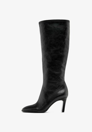Černá kožená vysoká bota po kolena s špičatou špičkou a úzkým vysokým podpatkem. Hladká textura s bezšvovým designem a bez viditelných kovových prvků.