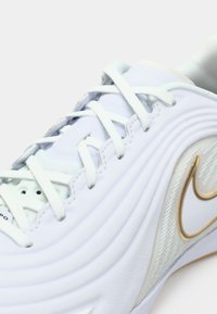 Λευκό αθλητικό παπούτσι με υφή από δέρμα στο επάνω μέρος, κορδόνια και χρυσή απόχρωση λογότυπου Nike. Διαθέτει διακριτικά κυματιστά σχέδια στο πλάι.