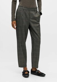 Pantalons à carreaux gris avec une taille haute, des jambes droites et une texture douce. Portés avec des chaussures plates noires ornées d'un nœud.