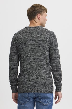 Grijze gebreide trui met een gemêleerd patroon, ronde hals en ribgebreide manchetten. Draagt over blauwe jeans, met een weergave van de achterzijde.