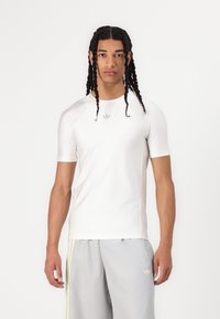 Balta sporta krekla ar īsām piedurknēm, uz kura krūtīm ir nemanāma adidas logo. Audums izskatās gluds un pieguļošs.