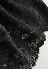 Black lace fabric with floral patterns and scalloped edges lying on a light surface, showing texture and intricate details.
